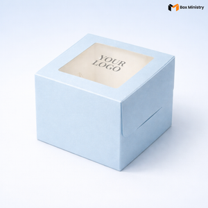 Soft sky blue square cake box with large square clear PVC window on lid showing "YOUR LOGO" text in elegant serif grey font centered on white interior base, positioned at 3/4 isometric angle, tall upright shape with prominently visible side walls, visible tuck-lock flap on right side face, matte finish, on a soft pale blue to white gradient background