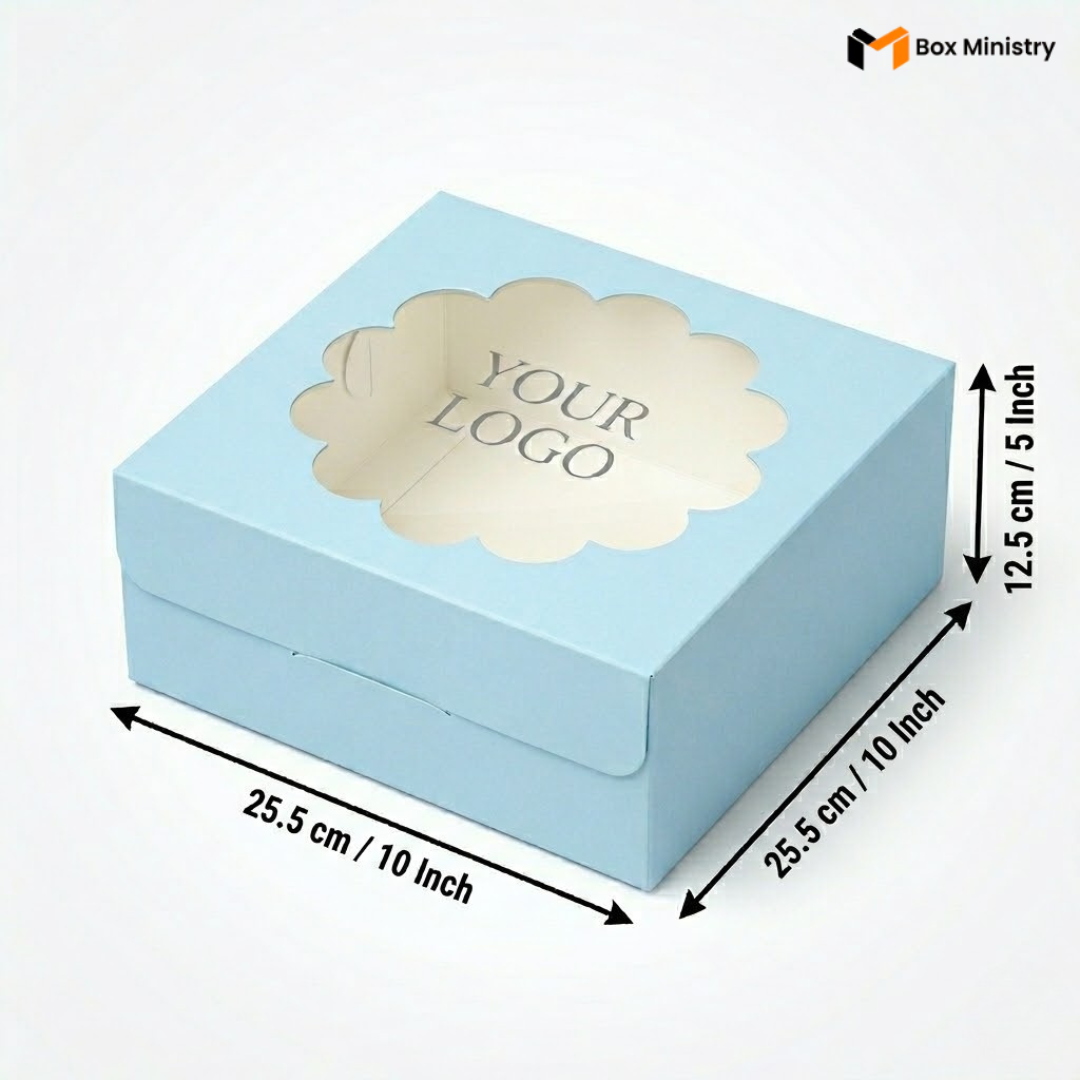 Soft sky blue square cake box with ornate flower-shaped scalloped petal PVC window showing "YOUR LOGO" text in elegant serif grey font, dimensions 25.5 x 25.5 x 12.5 cm (10 x 10 x 5 inches), shown in 3/4 isometric angle with bold black measurement arrows, visible side lock closure on front face, matte finish, on a soft light grey-white gradient background