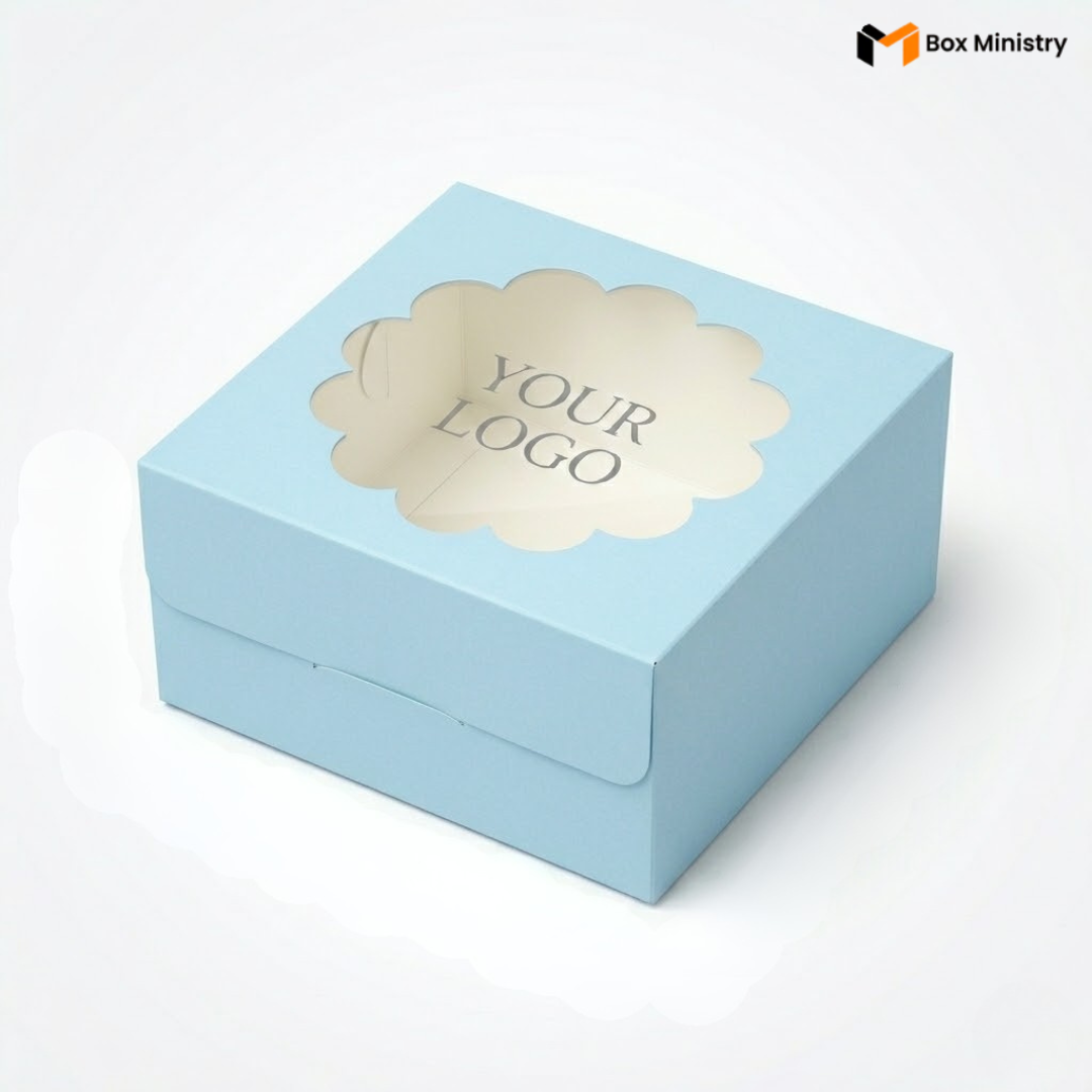 Soft sky blue square cake box with ornate flower-shaped scalloped petal PVC window on lid showing "YOUR LOGO" text in elegant serif grey font, positioned at 3/4 isometric angle, visible side lock closure on front face, matte finish, clean white interior visible through window, on a soft light grey-white gradient background