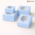 Four sky blue flower window cake boxes in two sizes arranged in a stacked tower layout on a soft cream background — small box stacked on top of large box on the left, two medium boxes on the right — Blue Flower Window Cake Boxes .