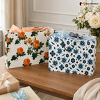Two floral-patterned gift bags on a wooden surface with a decorative box and flowers in the background.