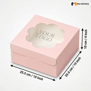 Soft blush pink square cake box with ornate flower-shaped scalloped petal PVC window showing "YOUR LOGO" text in elegant serif grey font on white interior base, dimensions 25.5 x 25.5 x 10 cm (10 x 10 x 4 inches), shown in 3/4 isometric angle with bold black measurement arrows on right and bottom edges, visible side lock closure on front face, flat matte pink finish, on a soft pure white background