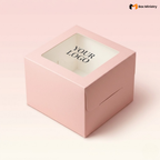 Soft blush pink square cake box with large square clear PVC window on lid showing "YOUR LOGO" text in elegant serif dark charcoal font centered on white interior base, positioned at 3/4 isometric angle, visible tuck-lock flap on right side face, tall upright shape with prominently visible side walls, matte finish, on a soft pale pink to warm white gradient background