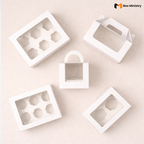White cupcake boxes in multiple sizes with window lids and gable handles, arranged in a flat lay product display
